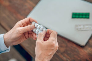 Person holding a blister pack of prescription steroid pills near a laptop, representing prednisone withdrawal symptoms and medication tapering.