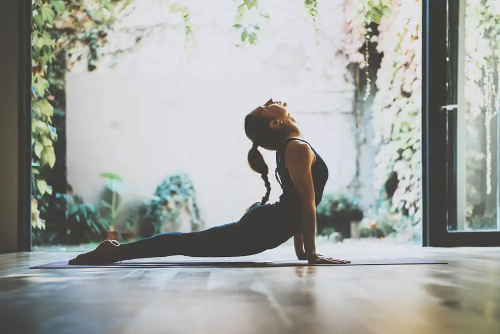 A woman in recovery is practicing yoga in a serene environment, surrounded by lush greenery and blooming flowers, promoting mental health and well-being. This peaceful setting encourages mindfulness and relaxation, which can be beneficial for those in recovery from substance use disorders and seeking long-term addiction treatment.