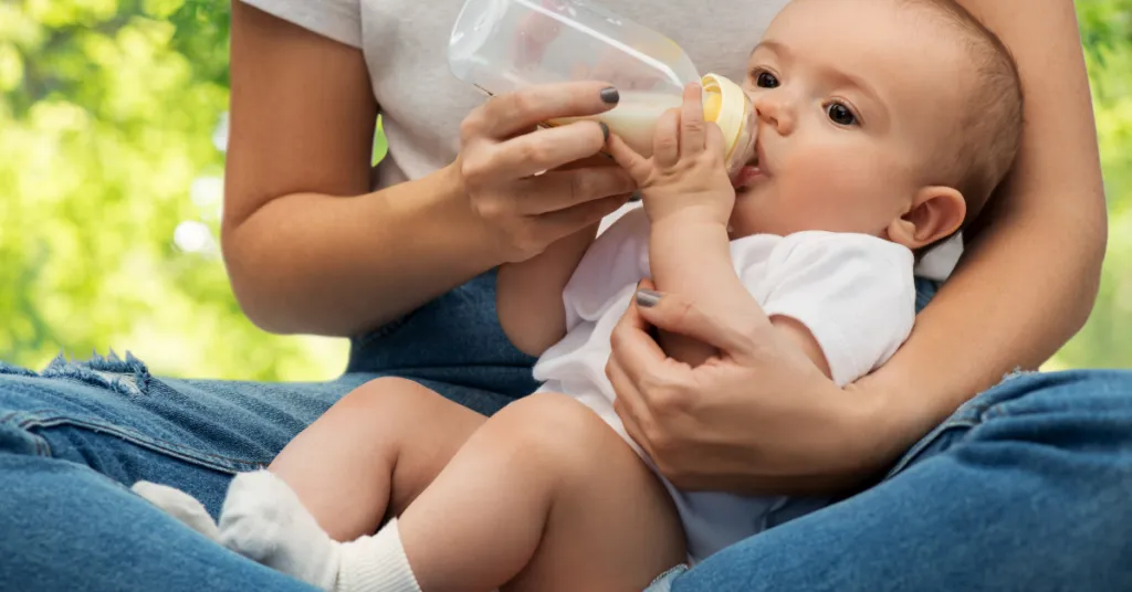 Mother feeding her baby with a bottle while sitting outdoors, illustrating alcohol and breastfeeding safety considerations.