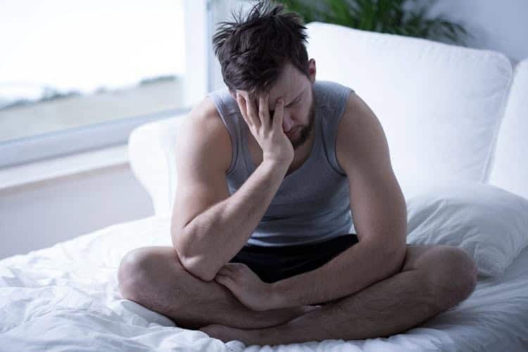 When You Reduce Your Alcohol Consumption Tired man holds head in hand while sitting on bed and dealing with alcohol withdrawal